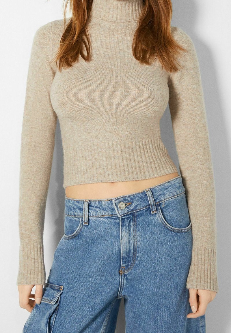 Beige ribbad polotröja med långa ärmar, kombinerad med högmidjade ljusblå jeans i denim med cargofickor.