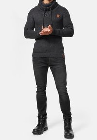 Pull en maille gris foncé avec un col châle haut et des cordons, associé à un jean noir ajusté et des bottes noires à lacets.