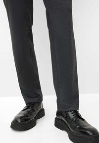 Grijze op maat gemaakte broeken van een geweven stof, gecombineerd met zwarte leren brogues met een dikke zool en decoratieve perforaties.
