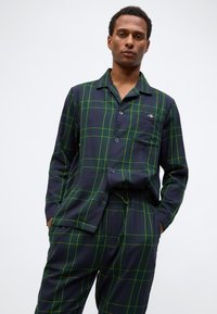 Set di pigiama a quadri navy con motivo a reticolo verde e giallo. Realizzato in tessuto morbido e leggero, con camicia con bottoni e pantaloni con vita elastica.