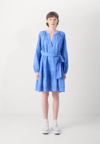 Rochie albastră cu mâneci lungi, guler în V adânc, legată cu o curea la talie, broderie florală, fustă cu volane, asortată cu adidași albi cu guler înalt.