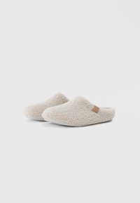 Vluchtige beige pantoffels met een zachte textuur, open achterkant en een klein leren accent aan de zijkant. Flexibele zool voor comfort.