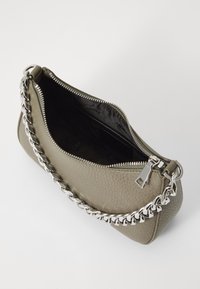 Olivnozeleni usnjeni ročni torbici z teksturirano površino, srebrno verižico in zadrgo. Notranjost je črna s subtilnim tiskom logotipa.