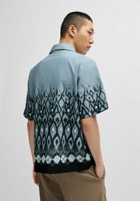 Camicia a maniche corte in tessuto azzurro chiaro con una sfumatura a motivo che presenta diamanti e design geometrici, che sfuma verso il nero all'orlo.