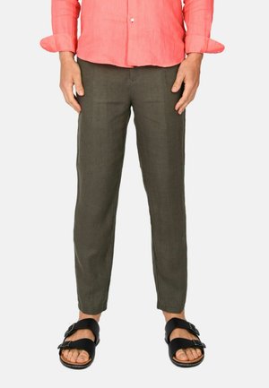 Pantaloni in lino verde oliva con vestibilità affusolata, abbinati a sandali neri con cinturini regolabili. La camicia è di colore corallo.