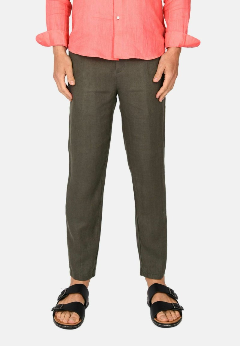 Pantaloni in lino verde oliva con vestibilità affusolata, abbinati a sandali neri con cinturini regolabili. La camicia è di colore corallo.