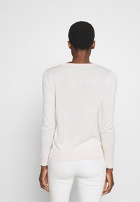 Lichtbeige lange mouwen trui met een ribbelzoom en manchetten, met een gladde, zachte textuur en een eenvoudig ontwerp. Achteraanzicht getoond.