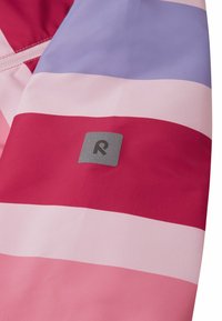 Veste imperméable avec des rayures horizontales en rose, rouge et lavande. Comprend une étiquette grise avec un logo stylisé en "R". Texture lisse.