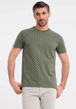 T-shirt verde a maniche corte con motivo a rombi color avorio. Design con colletto a girocollo e texture morbida. Indossato con pantaloni grigi chiari.