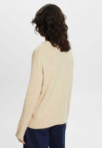 Licht beige oversized trui met een zachte textuur, verlaagde schouders en een ronde halslijn, van achteren getoond tegen een effen achtergrond.