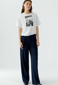 Witte katoenen t-shirt met een grafische druk met de tekst "ON THE ROAD," gecombineerd met donkerblauwe, gestreepte wijde broek en zwarte schoenen.