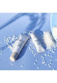 Two WASO Shiseido skincare tubes on blue surface surrounded by scattered white rice grains and a blue scoop filled with rice.