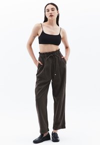Černý crop top, volné olivově zelené kalhoty s páskem na stažení, bočními kapsami a černými loafery. Hladká textura a uvolněný design.