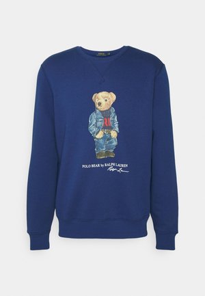 Marineblå sweatshirt med en bjørn iført denimjakke og jeans, stående, med teksten "Polo Bear by Ralph Lauren" under.