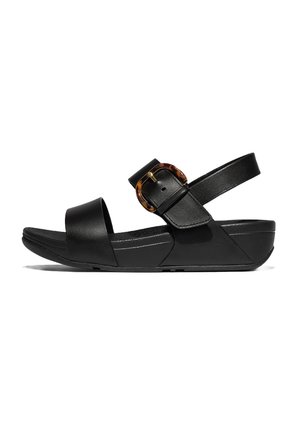 Sandales en cuir noir avec une large bride avant, une sangle de cheville ajustable et une boucle ronde en écaille de tortue. Semelle compensée légèrement surélevée.