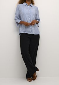 Blue and white striped button-up shirt with three-quarter sleeves, paired with wide-leg black trousers and brown heeled sandals.