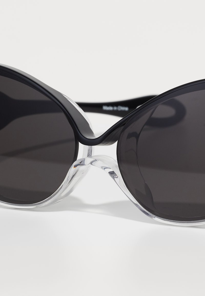 Occhiali da sole a forma di gatto neri con lenti scure, caratterizzati da una montatura in plastica trasparente e dettagli neri. Texture liscia, design moderno.