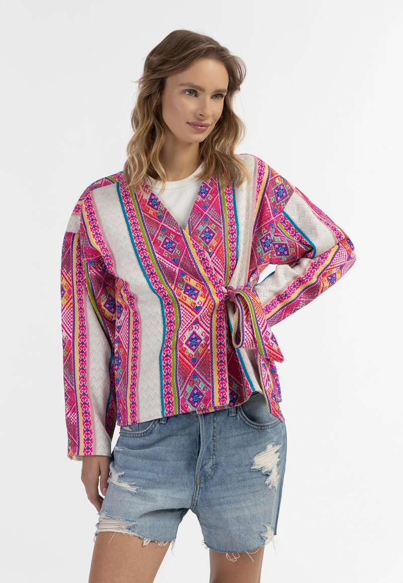 Krāsains kimono stila žakets ar dzīvīgu ģeometrisku rakstu rozā, zilā un dzeltenā krāsā, izgatavots no viegla auduma, ar garām piedurknēm un auklu.