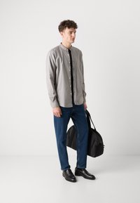 Lysegrå skjorte med knapper og svart plissér, kombinert med blå denimjeans og svarte lærsko. Holder en svart veske.