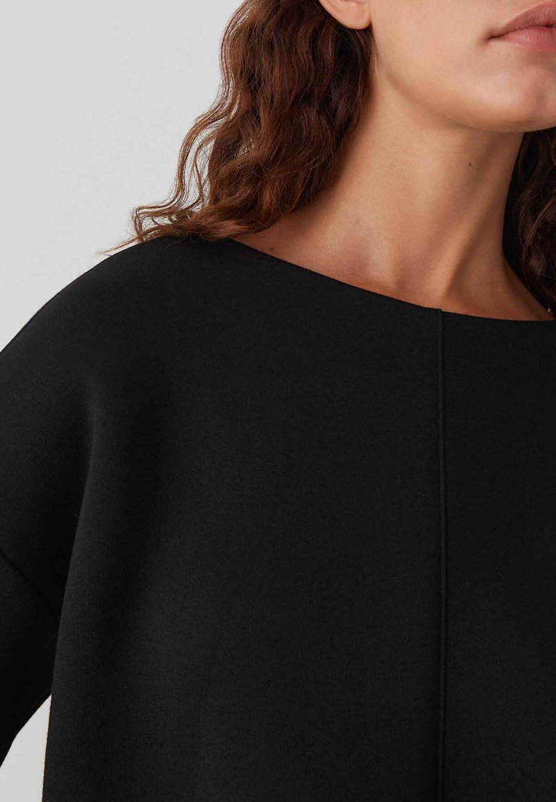 Maglione nero con ampio scollo a barca, texture morbida e dettagli di cucitura minimi. Il design presenta una vestibilità rilassata e oversize.