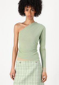Asymmetrische lange mouw top in lichtgroen, met geplooide textuur en een getailleerd silhouet, gecombineerd met een gestructureerde groene tweed rok.