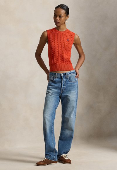 Πλεκτό πορτοκαλί γιλέκο χωρίς μανίκια με ριμπ στο τελείωμα, συνδυασμένο με ανοιχτό μπλε τζιν σε άνετη εφαρμογή και καφέ δερμάτινα παπούτσια με κορδόνια. Απλός σχεδιασμός και casual στυλ.