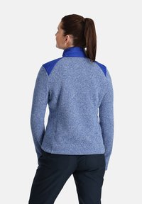 Giacca in pile blu con un design strutturato, caratterizzata da una spalla liscia blu e maniche testurizzate. Sul retro.