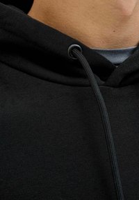 Musta huppu-sweater, jossa on ribbikuvioitu kaula-aukko, litteä nyöri ja sileä pinta. Lähikuva, joka näyttää kankaan ja hupun suunnittelun yksityiskohtia.