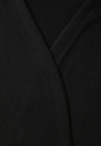 Primer plano de tela negra con textura de punto visible y una costura que se pliega en diagonal a través del encuadre.