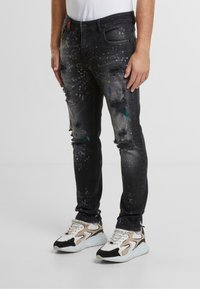 Czarne dżinsy z przetarciami i detalami w postaci plam farby. Dopasowany fason z kieszeniami i delikatnym połyskiem, zestawione z białymi i beżowymi sneakersami.