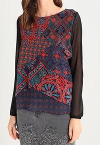 Blusa multicolore scura con intricati motivi geometrici e floreali, design a strati e maniche nere trasparenti.