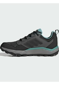 Zapato exterior negro con parte superior de malla texturizada, acentos turquesas y una suela gris robusta con profundos surcos para tracción.