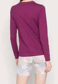 Långärmad lila T-shirt i mjuk bomull med rund halsringning, matchad med mönstrade pastellshorts med blå och rosa akvarellmönster.