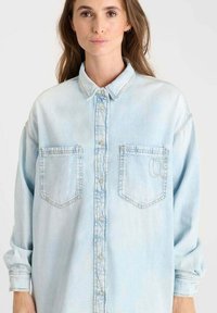 Lichtblauwe denim shirt met een knoopsluiting aan de voorkant, twee borstzakken en een relaxte pasvorm. Heeft een klassieke kraag en lange mouwen.