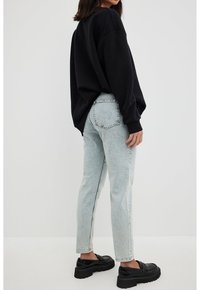 Sweatshirt noir décontracté, jeans bleu clair, et mocassins chunky noirs. Design simple, coupe décontractée, et texture de tissu douce.