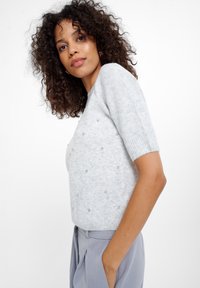 Lichtgrijze korte mouwen trui met een gestructureerde afwerking en kleine decoratieve kralen verspreid over de stof, gecombineerd met hooggetailleerde broek.