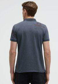 Dark gray polo shirt with short sleeves, featuring a textured pattern on shoulders and printed details near the collar. Cotton material.