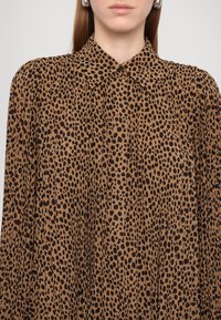 Brun blus med krage, som har ett leopardmönster i svart. Materialet verkar vara lättviktigt med plisserade detaljer.