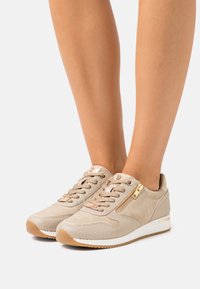 Baskets en daim beige avec des accents texturés, un détail de fermeture éclair dorée et une semelle en caoutchouc. Design à lacets avec une coupe basse et un bout arrondi.