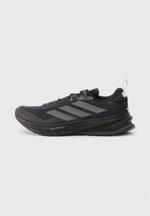 Chaussure de running noire Adidas avec des bandes grises, des lacets noirs et blancs, une semelle amortie et une languette au talon sur fond gris.