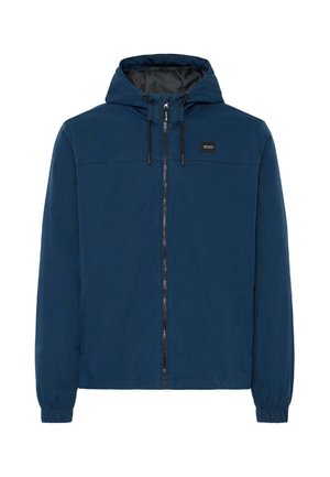 Chaqueta azul con capucha que presenta un cierre frontal con cremallera, puños elásticos y una placa de logo negra en el pecho. Textura de tela suave.