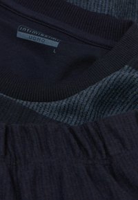 Dunkelblaue Kleidungsstücke mit gerippten Texturen. Die Etiketten tragen die Aufschrift "Intimissimi Uomo" in einem rechteckigen Muster, Größen sichtbar: L.
