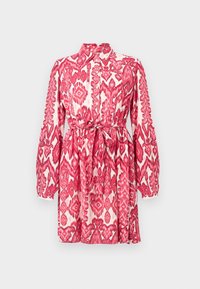 Robe courte à manches longues avec motif tribal rouge et blanc, col montant, boutonnière devant et ceinture à nouer à la taille sur fond neutre.