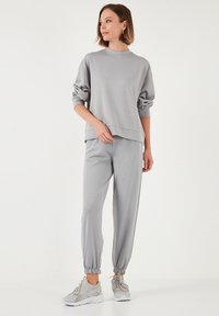 Grauer Pullover mit Rundhalsausschnitt und lockeren Ärmeln, kombiniert mit passenden grauen Jogginghosen mit elastischen Bündchen. Getragen mit hellgrauen Sneakers.