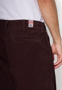 Hnědé kordové kalhoty s vertikálním žebrováním, vybavené zadní kapsou a štítkem Wrangler na pasu.
