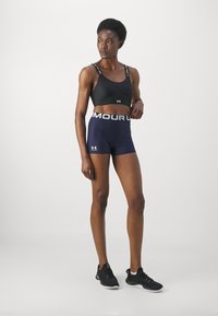 Zwarte sport-bh met logo-accenten; marineblauwe hoge shorts met een logo-elastische tailleband; gecombineerd met zwarte sportschoenen.
