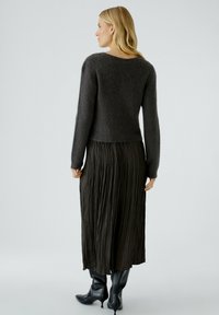 Pull en maille gris foncé avec un col rond, associé à une jupe maxi plissée noire et des bottes noires montantes. Design simple et texturé.