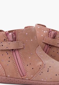 Stivaletti alla caviglia in suede rosa con spruzzi glitterati, dotati di cerniera laterale e fascia in velcro. Forma arrotondata e suola testurizzata per una buona aderenza.