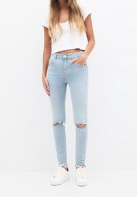 Ljust blå skinny jeans med slitna knän, fransade fållar och en mjuk denimtextur, matchat med vita sneakers och en kort topp.