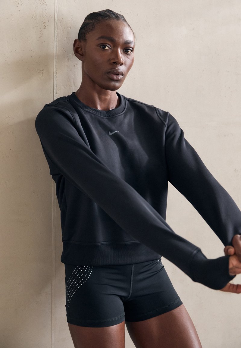 Zwarte sportieve sweatshirt met lange mouwen en een ronde halslijn, gecombineerd met zwarte shorts voorzien van decoratieve zilveren studs langs de zijkanten.